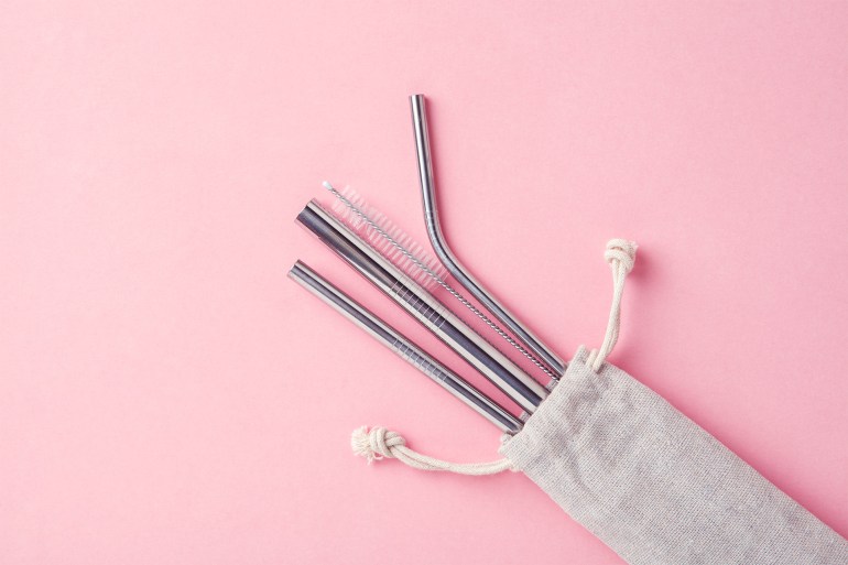 reusable stainless steel straws and cleaning brush in white cotton bag on pink background, eco friendly lifestyle