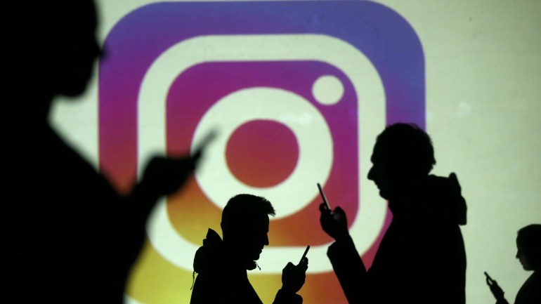 Silhouettes of mobile users are seen next to a screen projection of Instagram logo in this picture illustration taken March 28, 2018. REUTERS/Dado Ruvic/Illustration